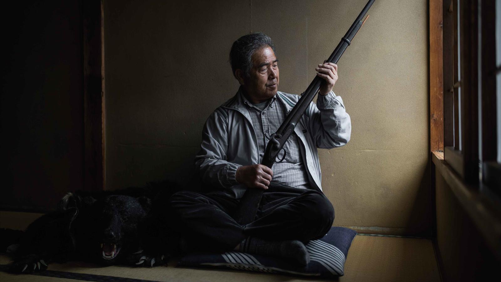 Endo-san sostenint un rifle que havien fet servir els seus ancestres i, al seu costat, una pell d’os negre japonès que decora l’habitació / Javier Corso / OAKstories